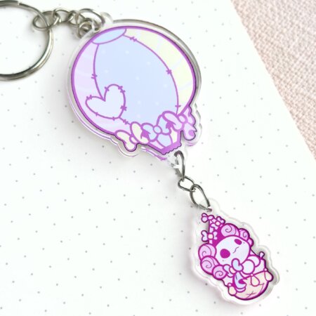 Cute axolotl keychain showing Evy's original cartoon character, Lottie the Lotl, travelling in a hot air balloon. The keychain has two charms: a hot air balloon and a Lottie.