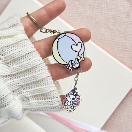 Cute axolotl keychain showing Evy's original cartoon character, Lottie the Lotl, travelling in a hot air balloon. The keychain has two charms: a hot air balloon and a Lottie.