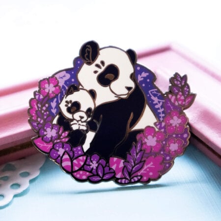 A lovely enamel pin presenting a panda mother with her cute panda cub. The two are presented in a semi-realistic art style, and sit surrounded by screen printed foliage. This panda pin is made from hard enamel and raised black nickel plated outlines.