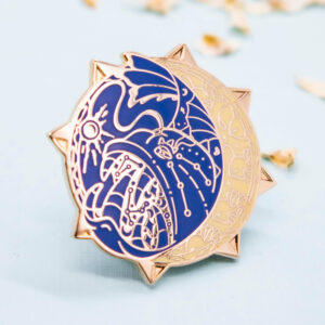 A hard enamel pin featuring a stylized (not cartoon style) deep-sea anglerfish. The enamel pin is framed by raised outlines plated with gold. The anglerfish pin has two colors: a deep blue and a warm yet subtle yellow. The color palette is inspired by early star charts and astronomy.