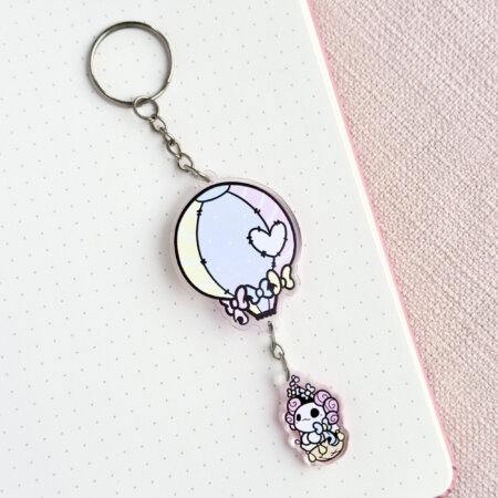 Cute axolotl keychain showing Evy's original cartoon character, Lottie the Lotl, travelling in a hot air balloon. The keychain has two charms: a hot air balloon and a Lottie.